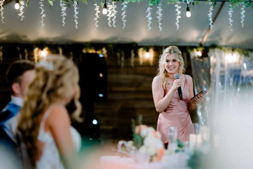 Maid of honor giving an emotional wedding reception speech, softly lit by off-camera flash and string lights