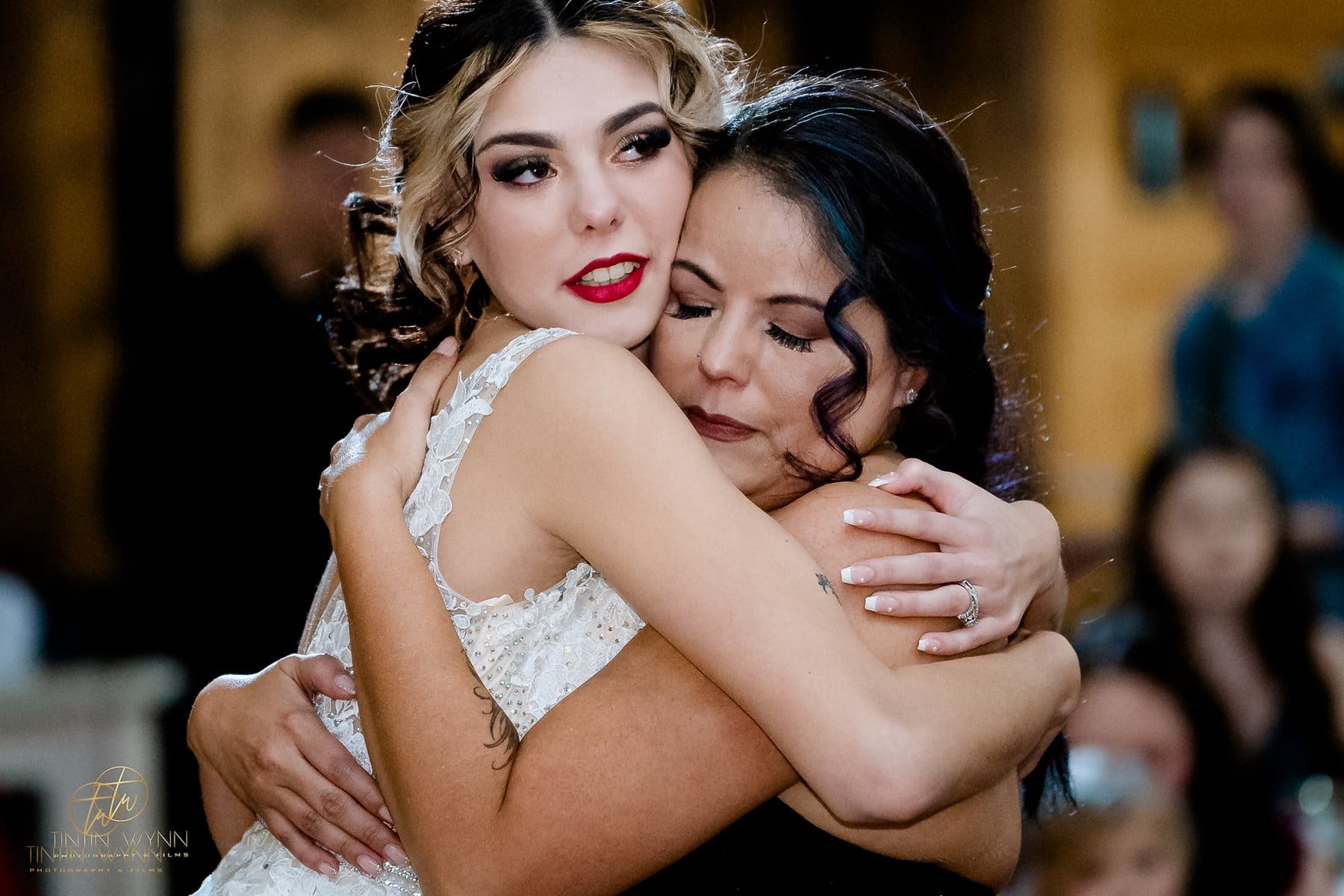 Leave Time for Loved Ones in Your Wedding Timeline Woman in a lace wedding dress embracing a woman with dark hair.